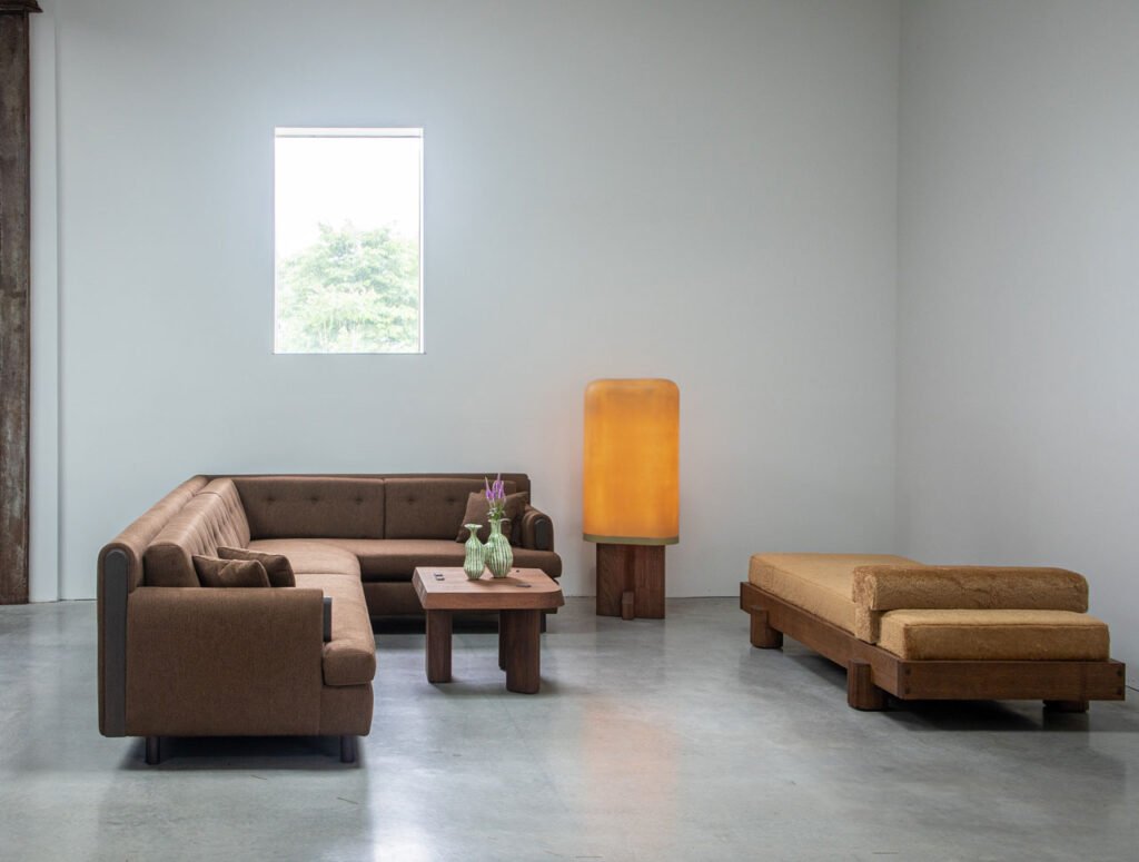 Minimalist living room with a brown sectional sofa, wooden coffee table, large glowing floor lamp, daybed, and a small window on a plain white wall—perfect inspiration for your next Friday Five.