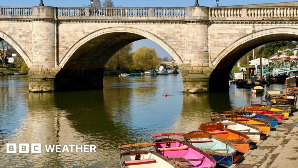 Sunshine reflecting off the water and bridge with a line of colourful row boats lined up on the bank