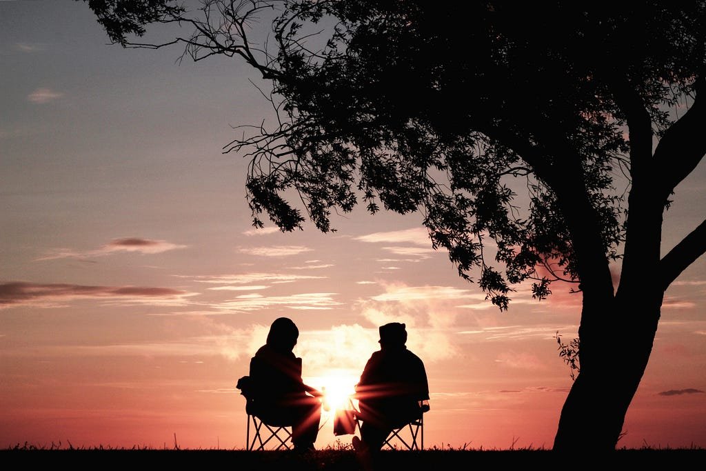Two figures sitting on chairs in the sunset (photograph)