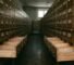 dim photograph of a long library card catalog corridor with rows of small wooden drawers labeled by hand, the drawers in the foreground pulled out and empty