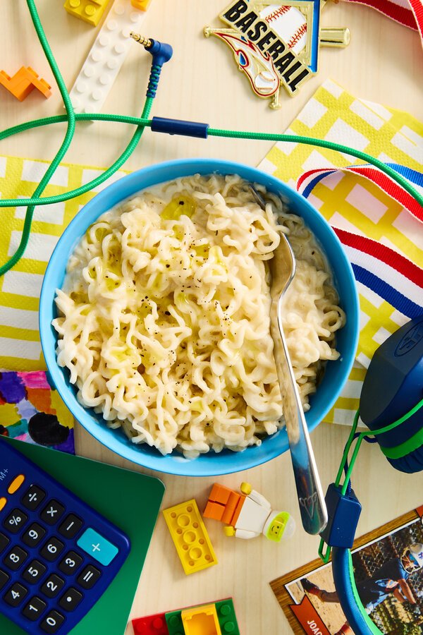 A bowl of chicken and kale topped with sliced avocado is surrounded by toys.