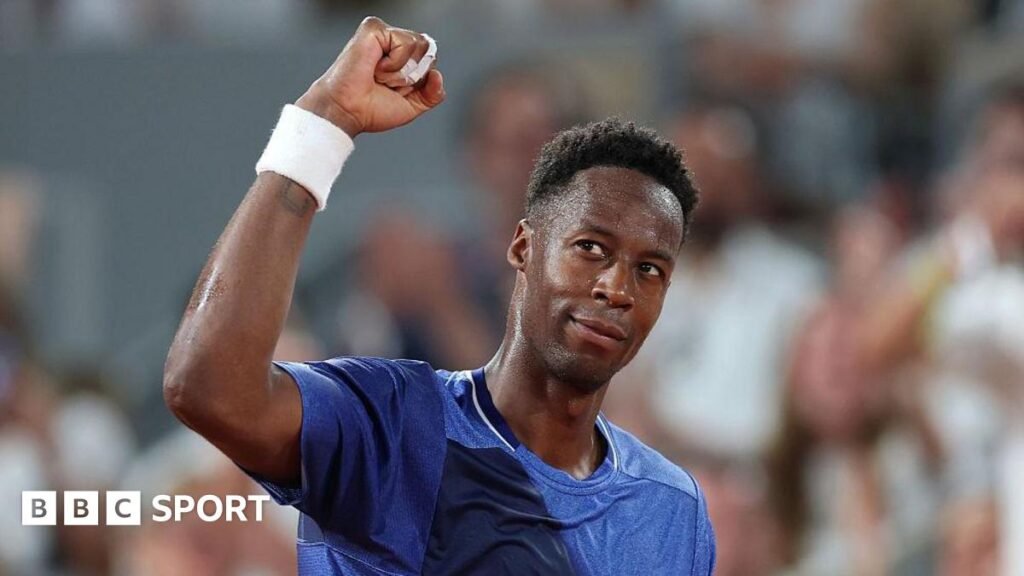 Gael Monfils, wearing a blue t-shirt, looks up to his right and raises his right fist