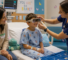 A child in a hospital gown sits on a bed wearing a VR headset, with a nurse adjusting the device and a parent watching beside them.