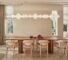 A modern dining room with a long wooden table, six upholstered chairs, a sculptural pendant light, and minimal table decor. Large windows let in natural light.