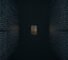 A cinematic, moody, high-end editorial shot with a 2:1 aspect ratio. The background is a vast, dark, out-of-focus wall of monospaced code that reads as abstract, cool blue-grey texture. In the center distance, a small, unreachable, door-shaped rectangle of warm amber light stands out against the darkness.