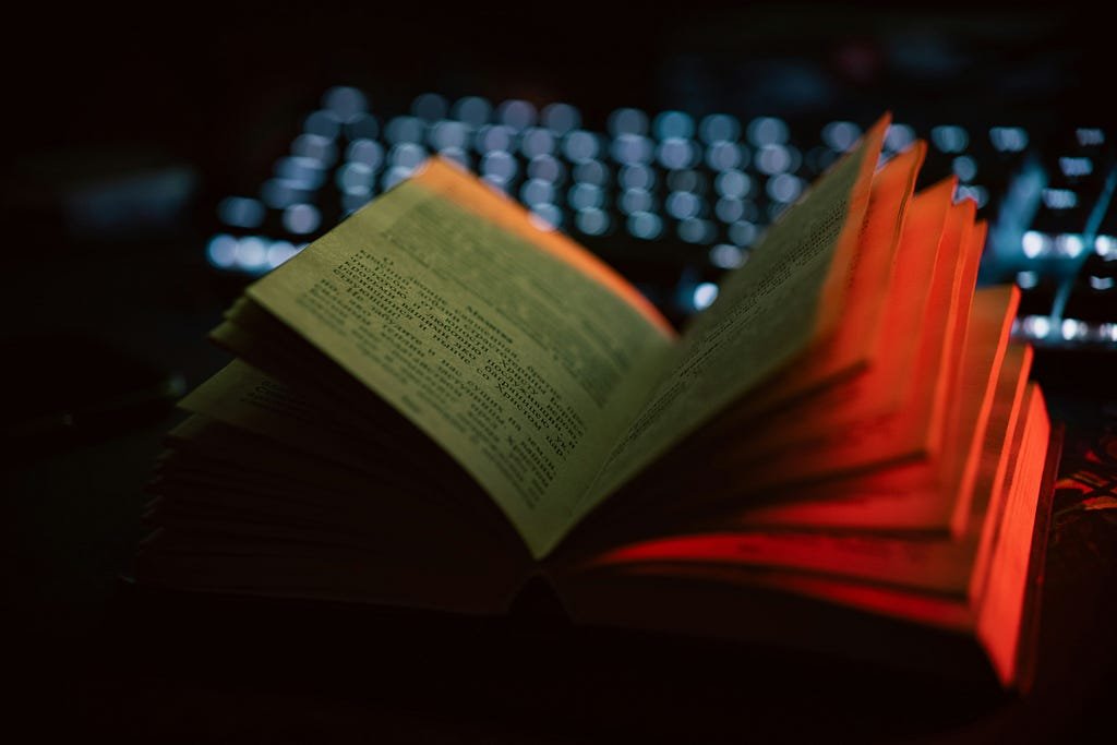 An open book illuminated by a red light, highlighting the text and pages for reading.