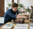 A design lead works on a screen alongside two designers at a shared table. AI assisted.